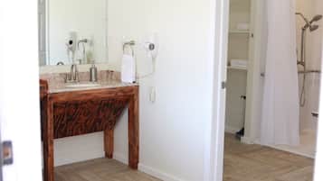 A bathroom with a wooden vanity, a mirror, a hairdryer, and a shower area.