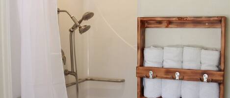 Una ducha con puerta de cristal, un perchero de madera con seis toallas y un cabezal de ducha.