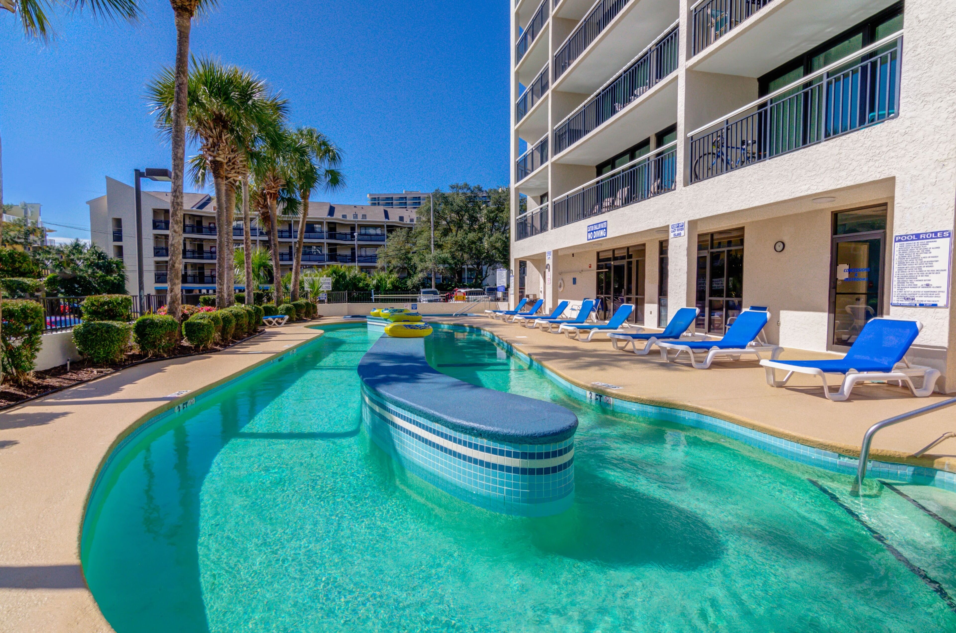 A swimming pool with blue lounge chairs and a building with balconies.