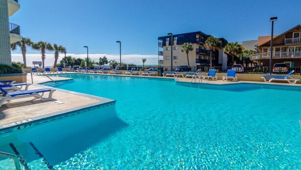 Una piscina azul cristalina con sillas de descanso y un edificio al fondo.