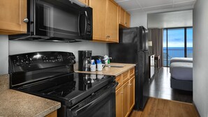 A compact kitchen with a stove, microwave, and refrigerator, wooden cabinets, and a view of the ocean through large windows. - Fantastic Efficiency w/ Great Oceanfront View+Official On-Site Rental Privileges (Myrtle Beach)