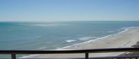 Une vue sur la plage depuis un balcon doté d’une balustrade, avec une plage de sable et l’océan en toile de fond.