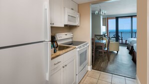 A kitchen with white cabinets, a microwave, and a stove. There is a dining area with a table and chairs, and a balcony with a view.