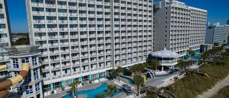 A large hotel with multiple floors, a swimming pool, and a beach area.