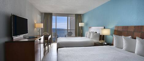 A hotel room with two beds, a desk with a TV, a chair, and a view of the sea.