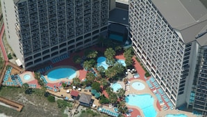 Vue aérienne d’un hôtel doté de plusieurs piscines, d’une plage et d’un parking.