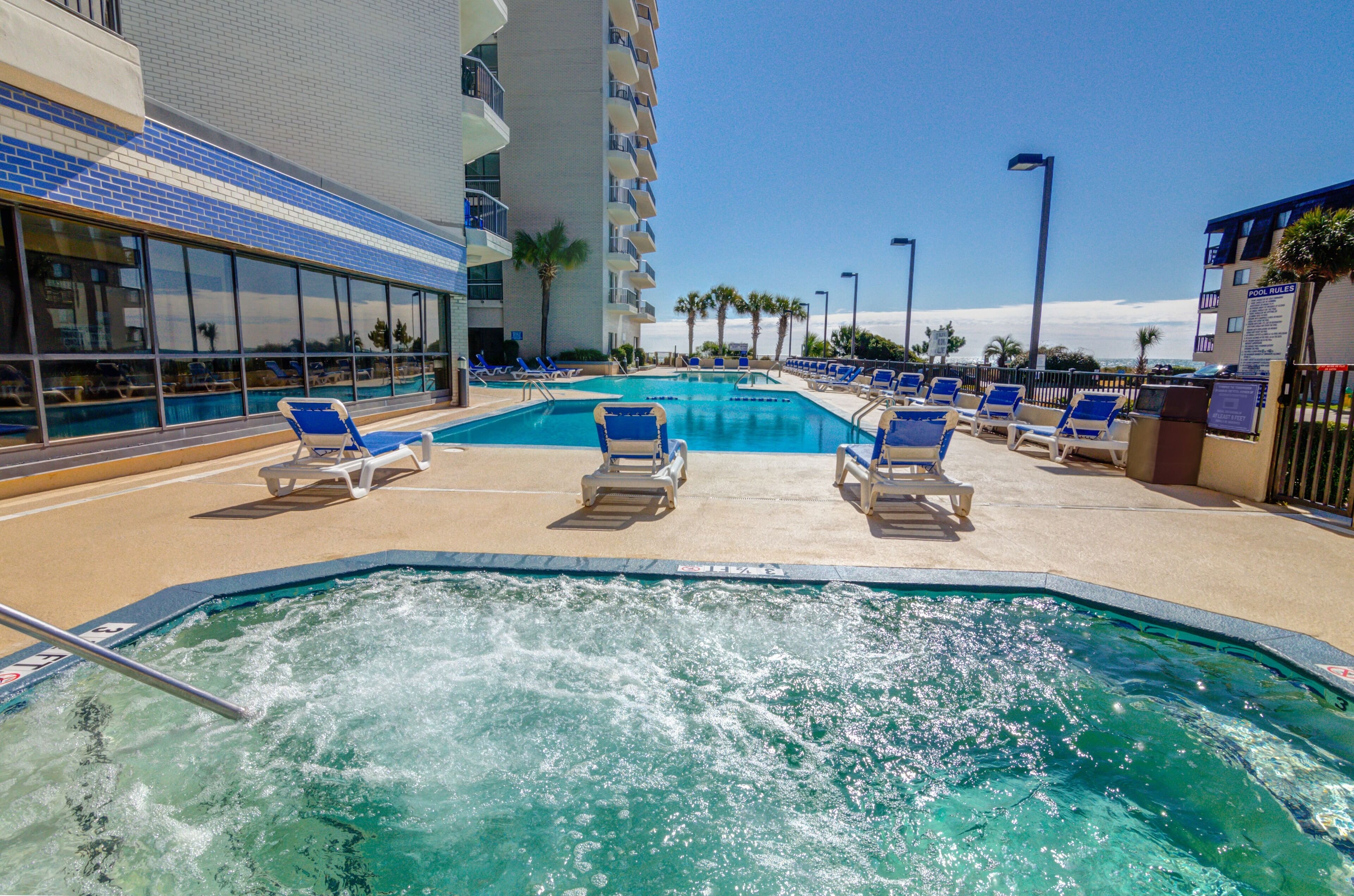 A pool area with blue lounge chairs and a hot tub.