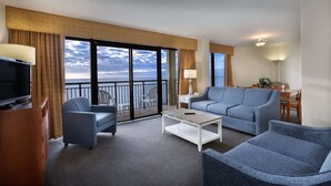 A hotel room with a balcony, a sofa, a chair, a TV, a lamp, and a dining table with chairs. - Oceanfront 2 Bedroom Condo w/ Great View + Official On-Site Rental Privileges (North Myrtle Beach)