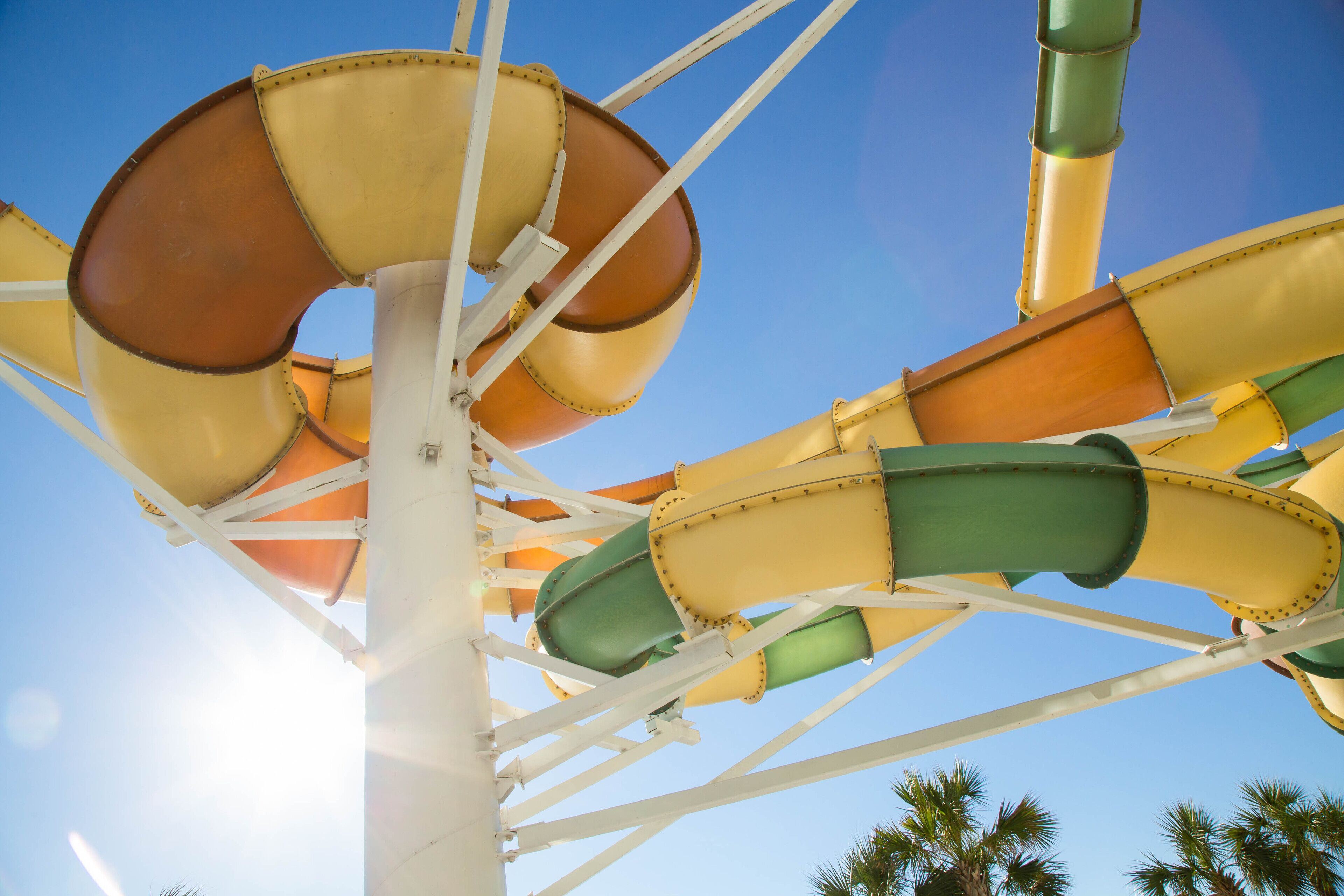 A water slide structure with multiple lanes, supported by a white metal frame, against a clear sky.