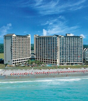 Un hotel frente a la playa con varios edificios altos, una playa de arena y un área de piscina.