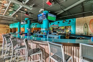 Zona de bar con varias pantallas, una barra y taburetes.