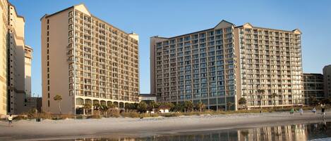 A beachfront hotel with multiple high-rise buildings, a sandy beach, and a calm sea.