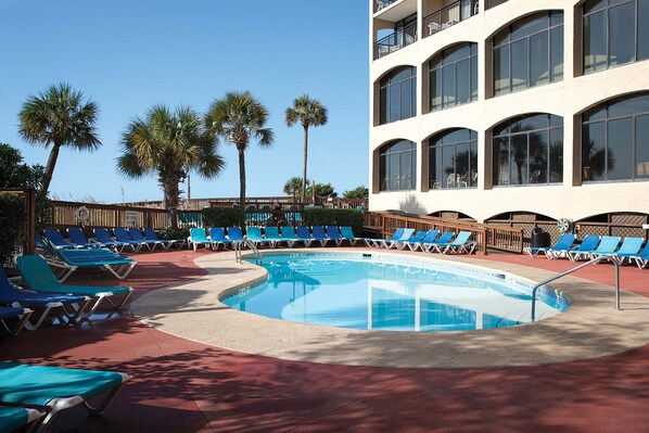A pool area with blue lounge chairs, a swimming pool, and palm trees.
