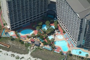 Eine Luftaufnahme eines Hotels mit mehreren Schwimmbecken, einem Strandbereich und einer Parkgarage.