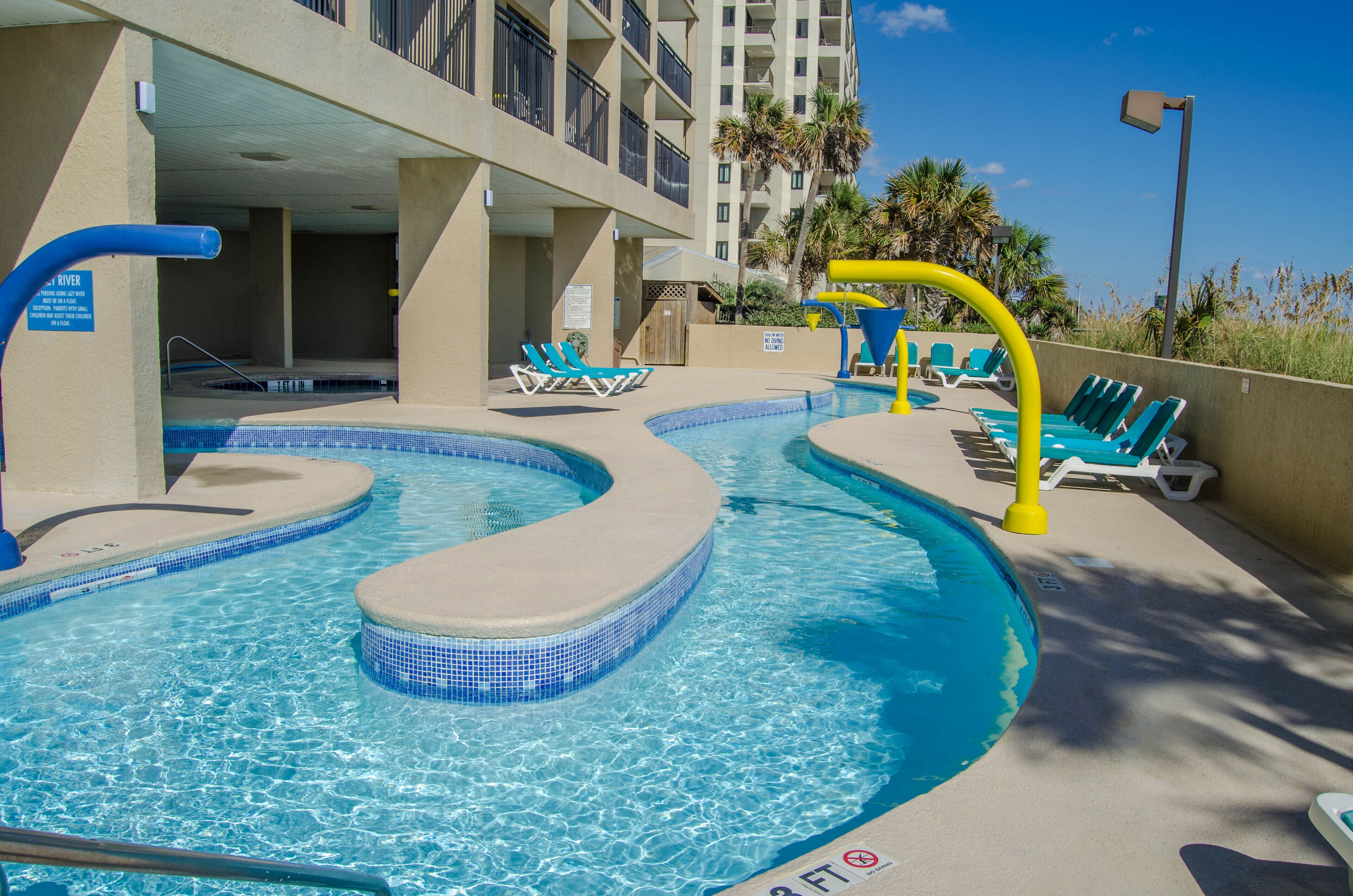 A pool area with multiple water features, including a hot tub and a water slide, surrounded by lounge chairs.