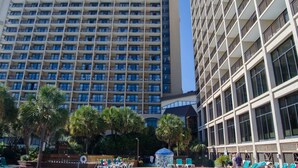 A high-rise hotel with multiple balconies and a pool area with lounge chairs and palm trees. - Oceanfront 1 Bedroom Suite w/ Gorgeous View + Official On-Site Rental Privileges (North Myrtle Beach)