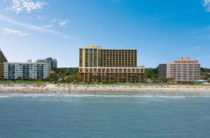 A beachfront hotel with multiple floors, a sandy beach, and a clear blue sky. - Oceanfront Suite w/ Fantastic View + Official On-Site Rental Privileges (Myrtle Beach)