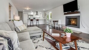 A modern living room with a sofa, coffee table, fireplace, and a kitchen in the background. - Downtown Kirkland - Luxury 3rd Street Retreat (Kirkland)