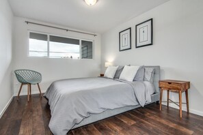 Ein Schlafzimmer mit einem Bett, einem Sessel, einem Nachttisch und zwei gerahmten Bildern an der Wand.