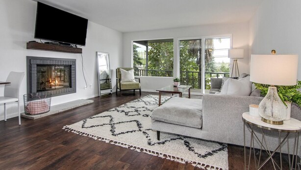 A modern living room with a fireplace, a large mirror, a sofa, and a view of greenery outside. - Downtown Kirkland - Luxury 3rd Street Retreat (Kirkland)