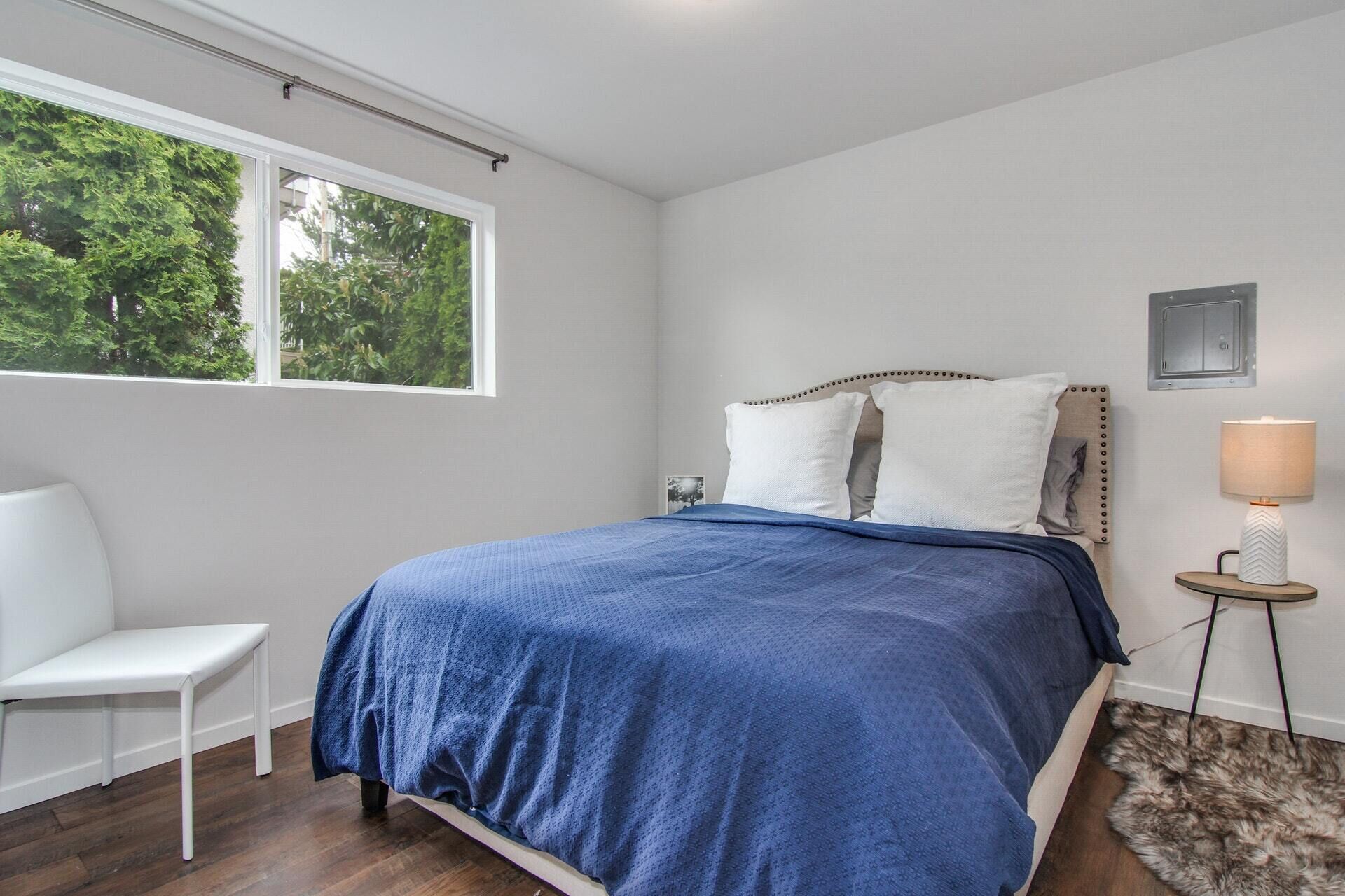 A bedroom with a bed, a chair, a lamp, and a view of trees through a window.