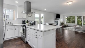 A modern kitchen with white cabinetry, a central island, stainless steel appliances, and a large window providing natural light. - Downtown Kirkland - Luxury 3rd Street Retreat (Kirkland)