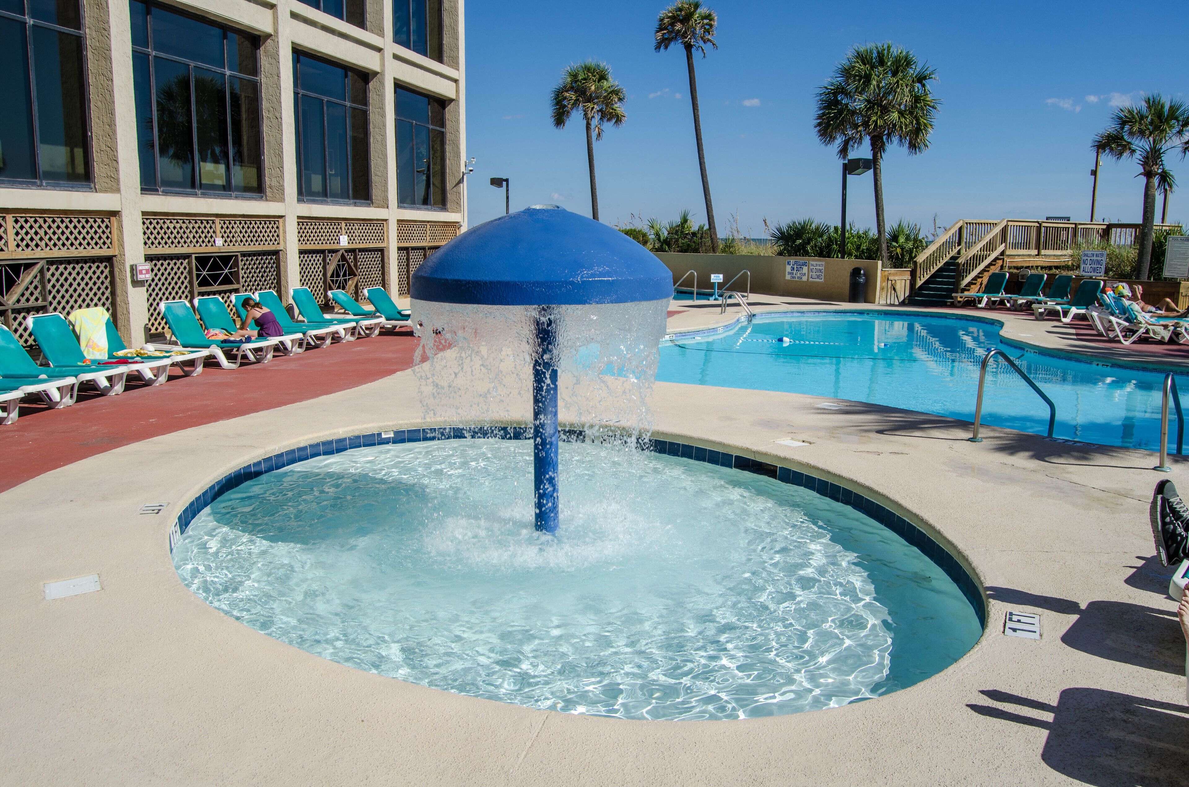 A pool area with a water feature, lounge chairs, and palm trees.