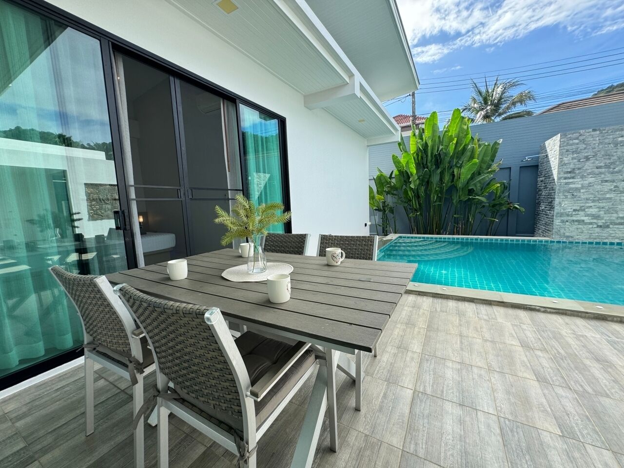 Un patio exterior con piscina, una mesa de comedor con sillas y un amplio ventanal con vistas a la piscina.