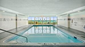 Ein Hallenbad mit Blick auf den Ozean durch große Fenster, ein Rettungsschwimmerstuhl und eine Poolleiter.