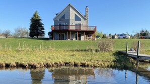 A house with a large deck, a stone chimney, and a pond in the foreground.