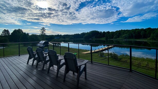 A deck with outdoor furniture overlooking a lake, a grill, and a wooden dock.
