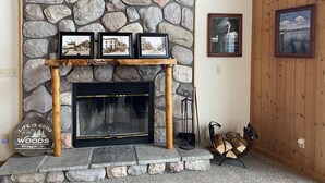 A stone fireplace with three framed pictures above it, a log holder, and a framed picture on the wall.