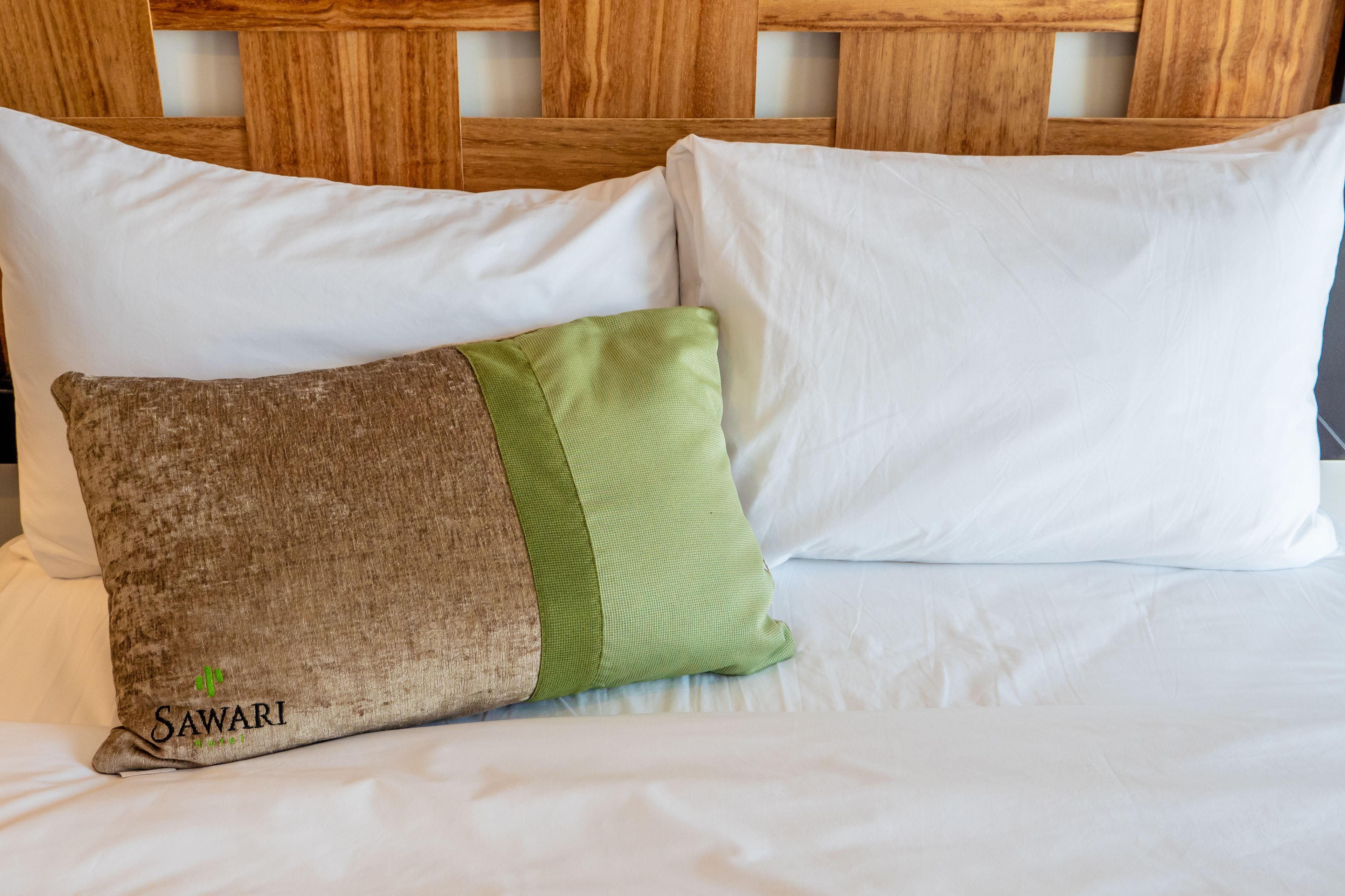 Ein Bett mit weißer Bettwäsche und zwei Kissen, eines mit einem grünen und braunen Muster.