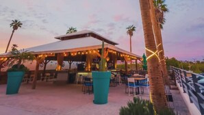 An outdoor patio area with a covered seating area, palm trees, and string lights. - Sawari Hotel (San Carlos)