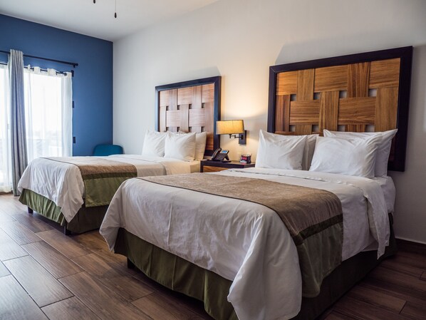 A hotel room with two beds, a nightstand with a lamp, and a blue wall.