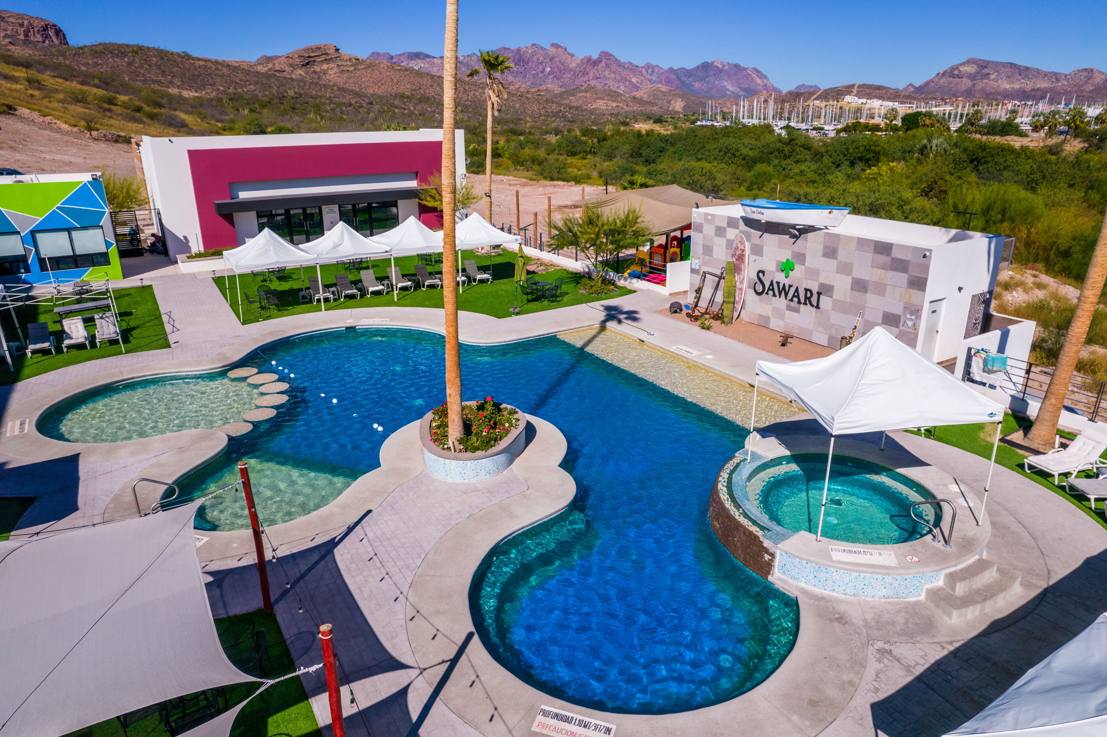Un resort con varias piscinas, un edificio moderno y vistas a montañas.