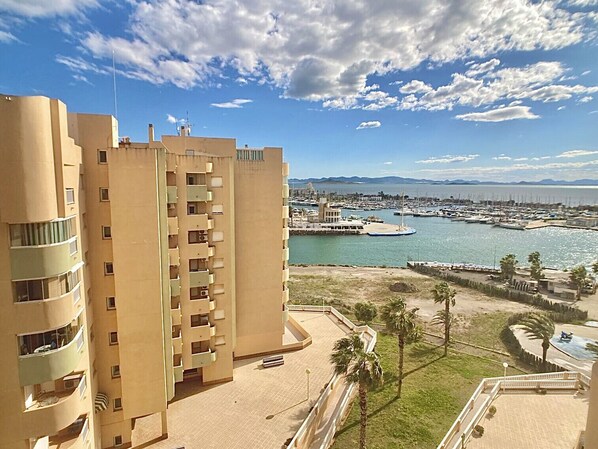 A high-rise building with multiple balconies, a marina with boats, and a clear sky.
