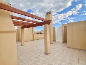 A rooftop terrace with a pergola structure, tiled flooring, and a white door.