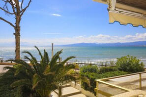 A balcony with a view of the sea, a palm tree, and a building with a balcony. - PLAYAMERO Apartment - Only Families (Salou)