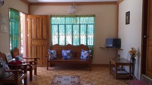 Un salon avec un canapé en bois, une table en bois, un téléviseur posé sur un meuble et un ventilateur.
