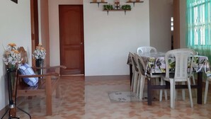 Un coin repas avec un sol carrelé, une porte en bois, une table avec des chaises et une étagère murale agrémentée d’objets décoratifs.