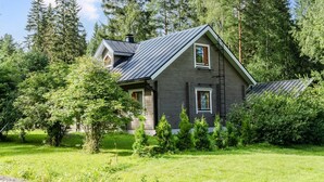 A two-story house with a dark grey exterior, a sloped roof, and a chimney. It is surrounded by lush greenery and trees. - Welhotar by Interhome (Lieksa)