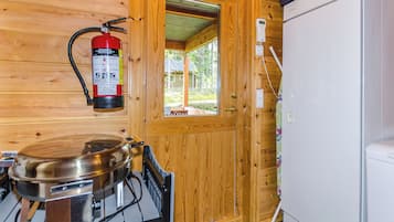 A wooden interior with a fire extinguisher mounted on the wall, a stove, a refrigerator, and a window leading to an outdoor area.