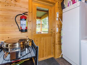 Een houten interieur met een brandblusser aan de muur, een fornuis, een koelkast en een raam dat uitkomt op een buitenruimte.