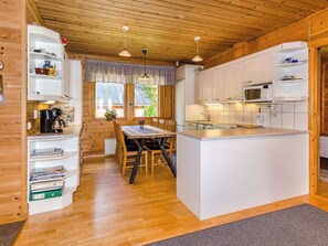 Een kleine keuken met een centraal eiland, houten kastjes en een eethoek met een tafel en stoelen.