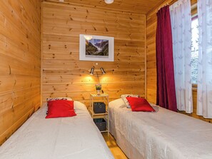 A wooden cabin room with two beds, a nightstand with a lamp, and a framed picture on the wall.