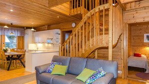 A cozy cabin interior with a gray sofa, wooden staircase, and a kitchen area. - Welhotar by Interhome (Lieksa)