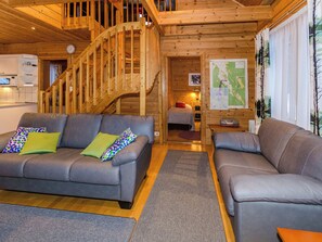 A cozy cabin interior with a wooden staircase, a sofa set, a dining area, and a map on the wall.