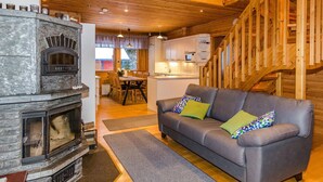A cozy living room with a stone fireplace, a gray sofa with colorful cushions, and a wooden staircase. - Welhotar by Interhome (Lieksa)