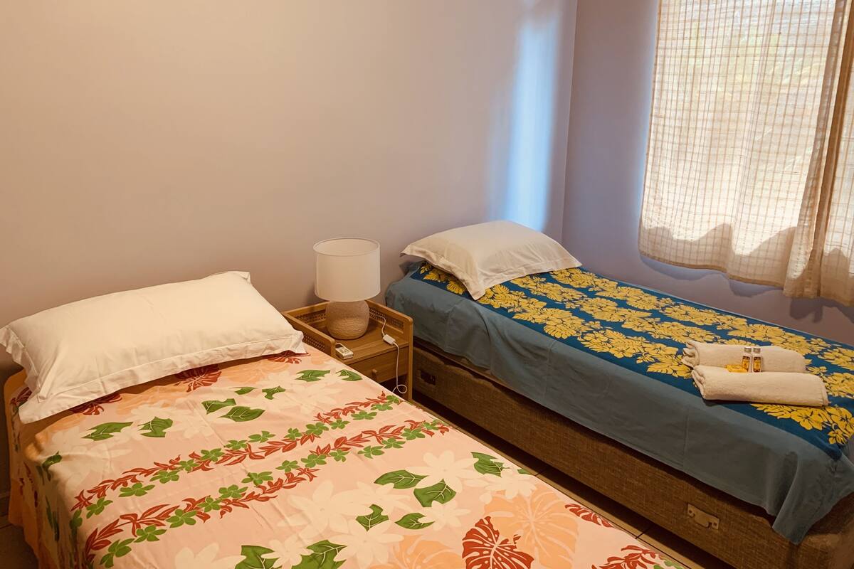 A bedroom with two beds, each with a different patterned bedspread. There is a nightstand with a lamp and a power outlet between the beds.